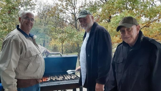 Three gentlemen standing outside at a grill.